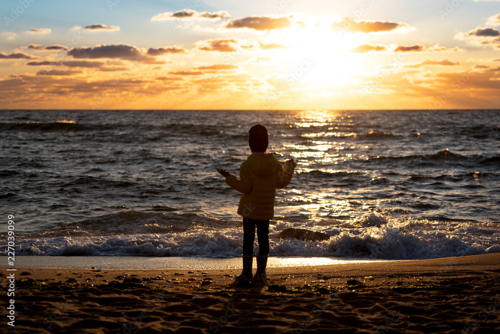 Little girl standing on the beach at the sunset time.
