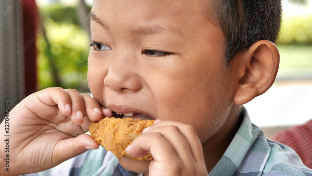 Cute asian boy are happy eating fried chicken leg in restaurant Cute asian boy are happy eating fried chicken leg in restaurant