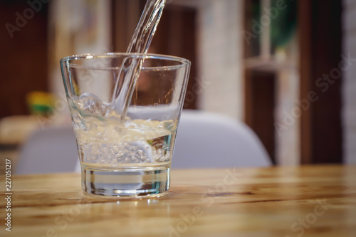 A glass of pure fresh water is poured into a glass, the background dinning room