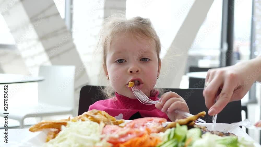 Cute little child girl eating french fries potato in fast food cort Cute little child girl eating french fries potato in fast food cort