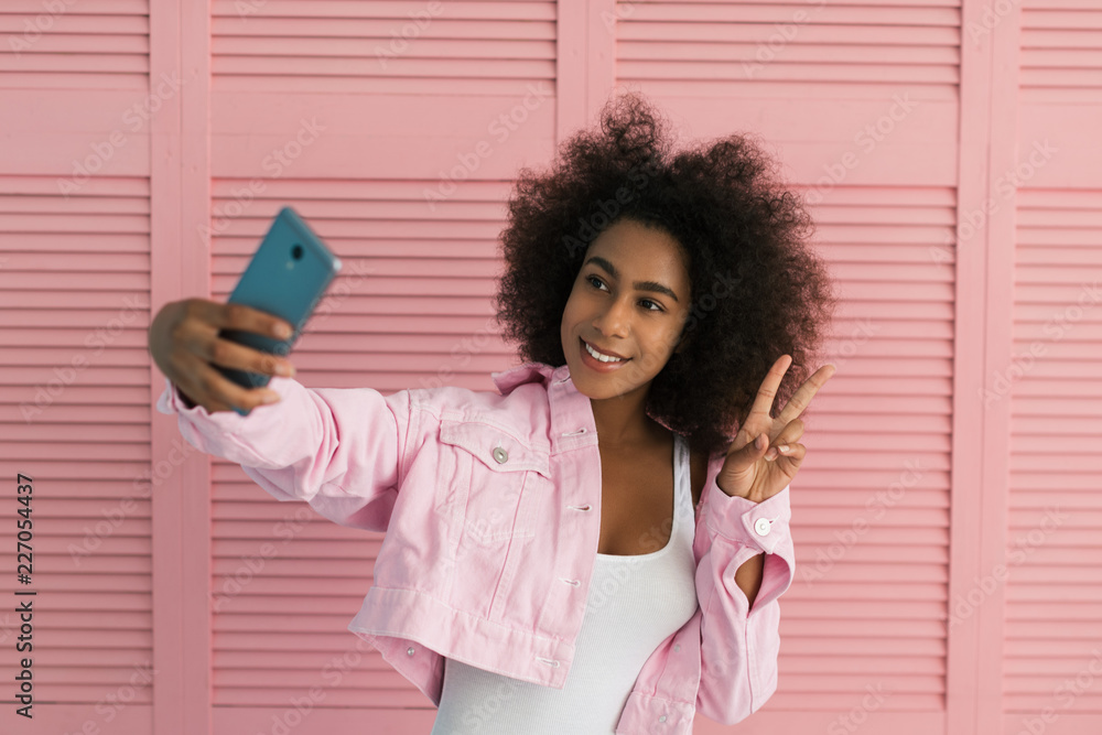 Positive happy African American woman with beautiful face and smile using  smartphone, taking selfies. Young hipster blogger wearing sexy bodice,  trendy pink jeans jacket streaming video online Stock Photo | Adobe Stock