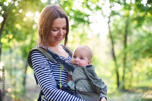 Mother with ergobaby carrying toddler in the forest photo