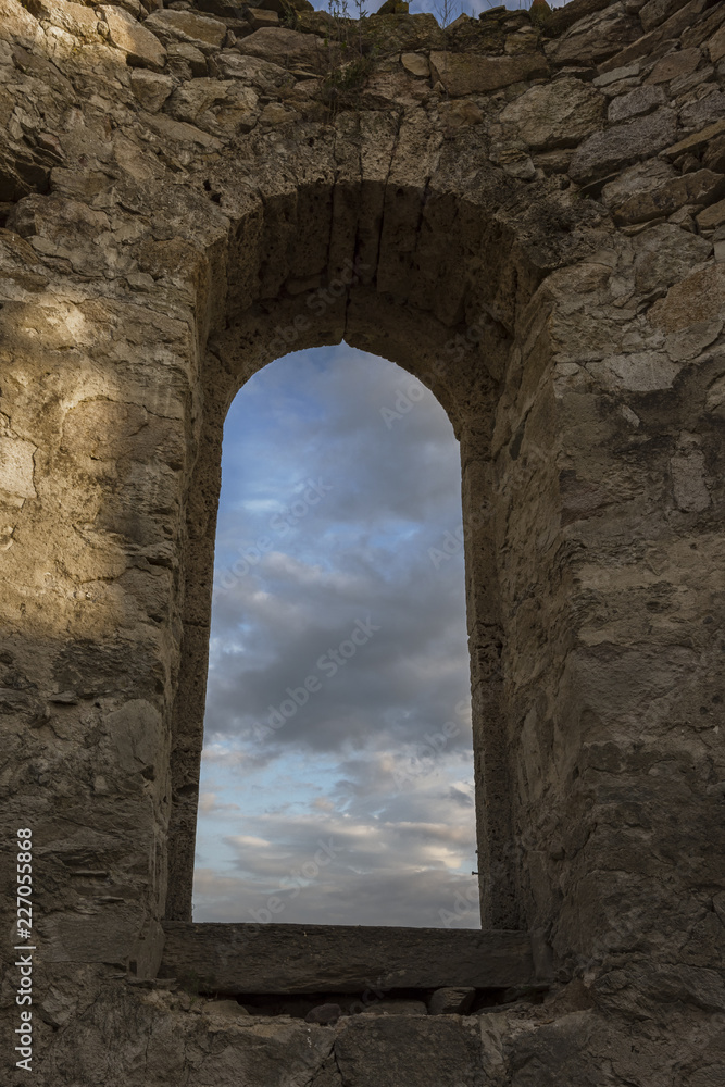 Beautiful colorful clouds on blue sky on sunset. View through arched window in old stone abandoned church. Аrchitecture concept.