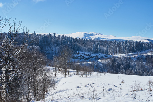 Panoramic view of the mountains. In the foreground there is a snow-covered glade, on the middle a forest, on the far a cliff, on the background. The Main Caucasian Ridge, Russia