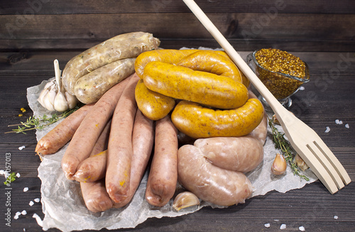 Assorted raw sausages with spices, vegetables and mustard on crumpled paper on a wooden table. photo