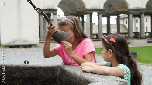 OROPA, BIELLA, ITALY - JULY 7, 2018: girls kids drink silver alpine water from silver buckets, from stone gothic mask fountain in Shrine of Oropa, Sanctuary, in the mountains near the city of Biella photo