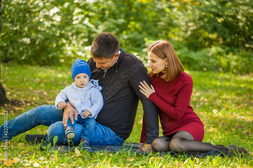 mom, dad and baby are sitting on the grass in the park. Family weekend in the fall © izida1991