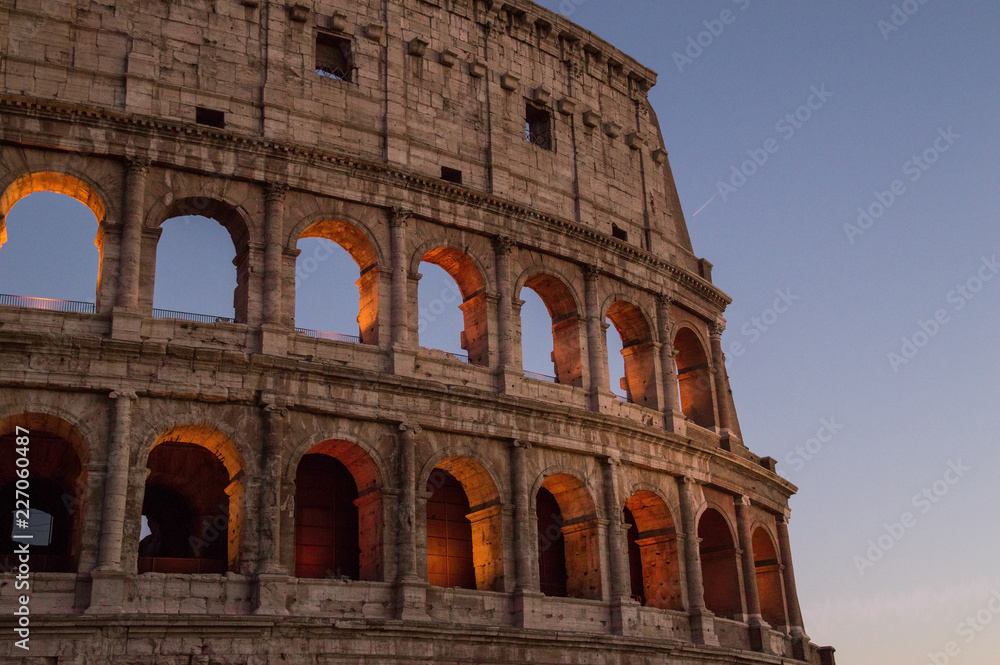 Colosseum, Rome, Italy. The outer wall of the evening coliseum. Arched openings are highlighted in orange backlighting. Evening cloudless sky on the background.
