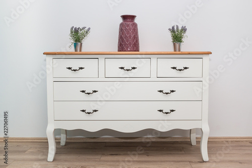 White wooden dresser with three vases and flowers on white wall background. Chest of drawers close up. photo