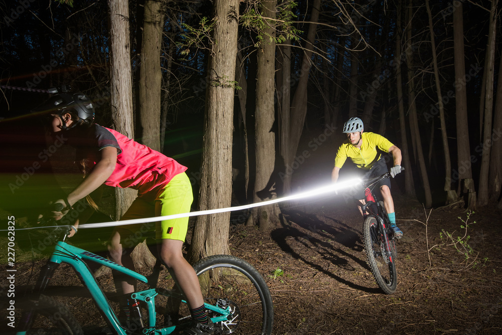 Man and woman riding mountain bikes at night with lights.