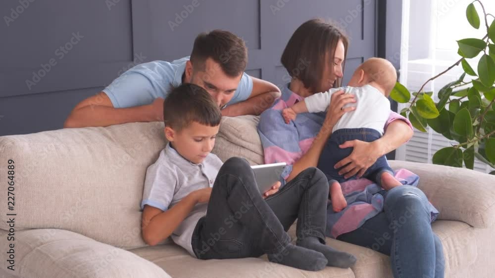Father and son staring at digital tablet while mother playing with small daughter Father and son staring at digital tablet while mother playing with small daughter