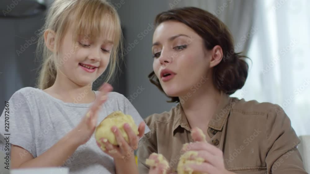 Close-up of happy mother and little daughter kneading dough and talking while cooking together in the kitchen Close-up of happy mother and little daughter kneading dough and talking while cooking together in the kitchen