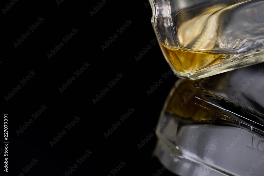 The last drop on the whiskey bottle close up on dark background, shiny reflecting surface.