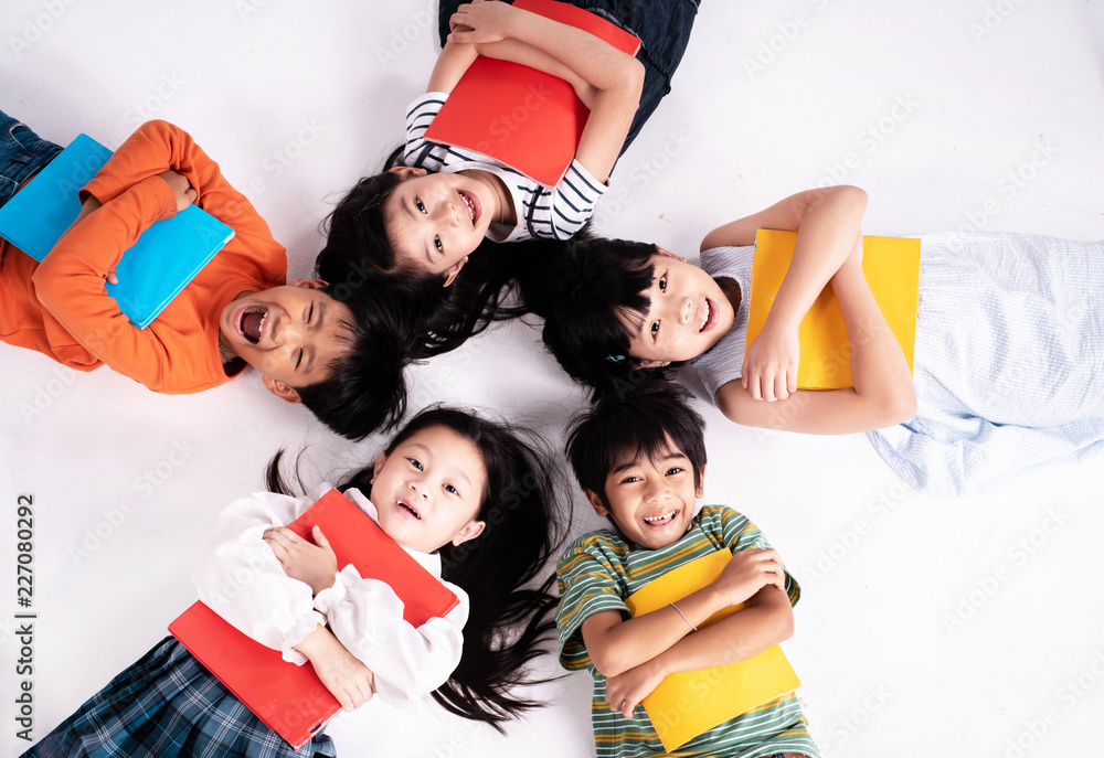 Fototapeta premium Kids are laying down on ground floor,holding book in hand with smile and happy face