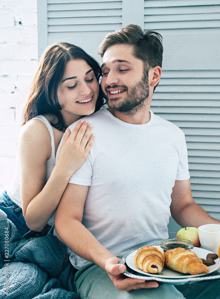 Happy beautiful cute couple in bedroom, they are eating a romantic  breakfast in bed while they kissing, hugging and relaxing together. Love,  relationships, family and St. Valentines day Stock Photo