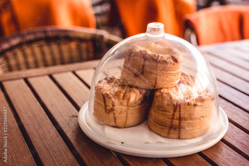 A small round pastry as a snack in a restaurant, a compliment from the chef, a Hungarian restaurant and cafe has such a service, a European tradition, plate with transparent cap on the wooden table