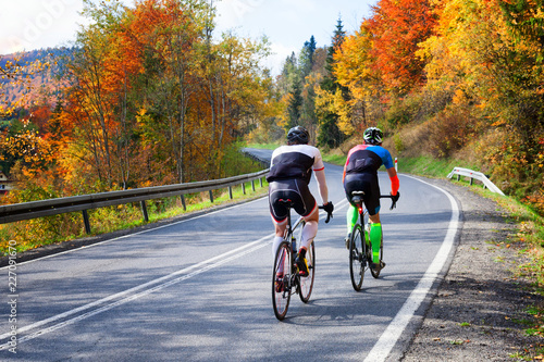 Fototapeta Naklejka Na Ścianę i Meble -  Cyclists on a trip in the autumn scenery. Autumnal landscape. Colorful leaves of trees.