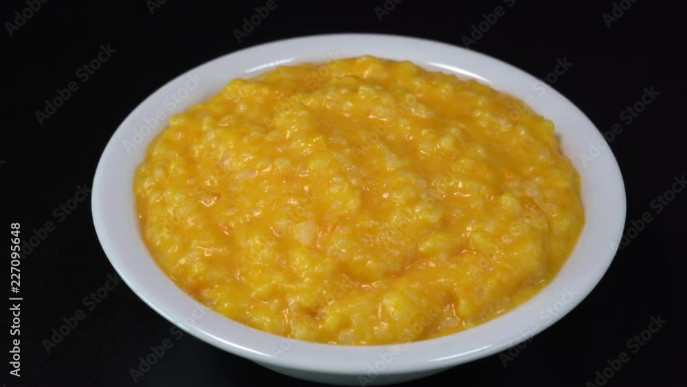 Pumpkin porridge with rice, milk, vanilla and sugar in a plate rotates on a black background. Close up, macro, 4k. Organic food Pumpkin porridge with rice, milk, vanilla and sugar in a plate rotates on a black background. Close up, macro, 4k. Organic food