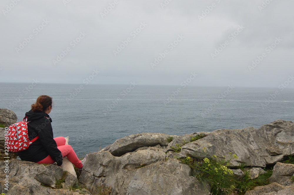 Beautiful Woman Looks At The Infinity Of The Cantabrian Sea From The Top Of Gulpiyuri Beach In The Council Of Llanes. Nature, Travel, Landscapes, Beaches. July 31, 2018. Llanes, Asturias, Spain.