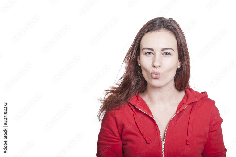 brunette woman makes a facial expression sharpening her lips to a kiss. she wears a red shirt and stands isolated on white background brunette woman makes a facial expression sharpening her lips to a kiss. she wears a red shirt and stands isolated on white background