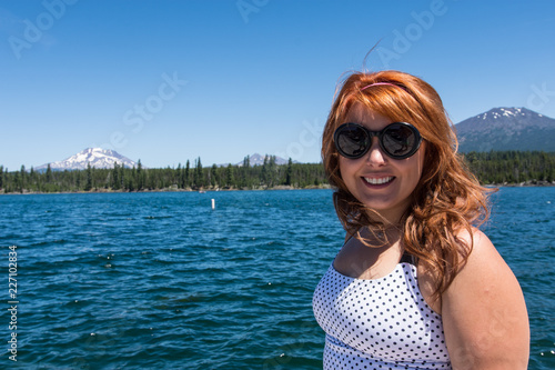 Pretty red hair female adult poses by Lava Lake along the Cascade Lakes Scenic Byway near Bend, Oregon. Mt. Bachelor in the distance © MelissaMN
