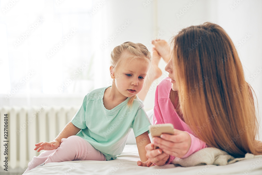 Young mother and her baby daughter using smart phone in bed Young mother and her baby daughter using smart phone in bed
