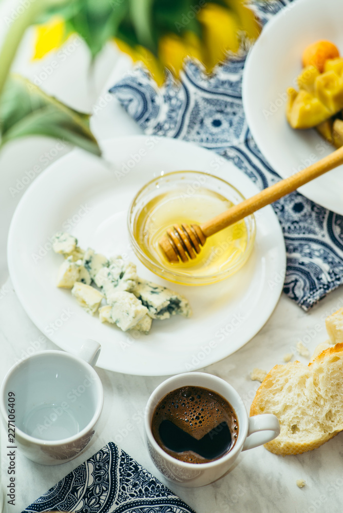 couple of cups with coffee, cheese, honey, baguette and fruit on a light marble table couple of cups with coffee, cheese, honey, baguette and fruit on a light marble table