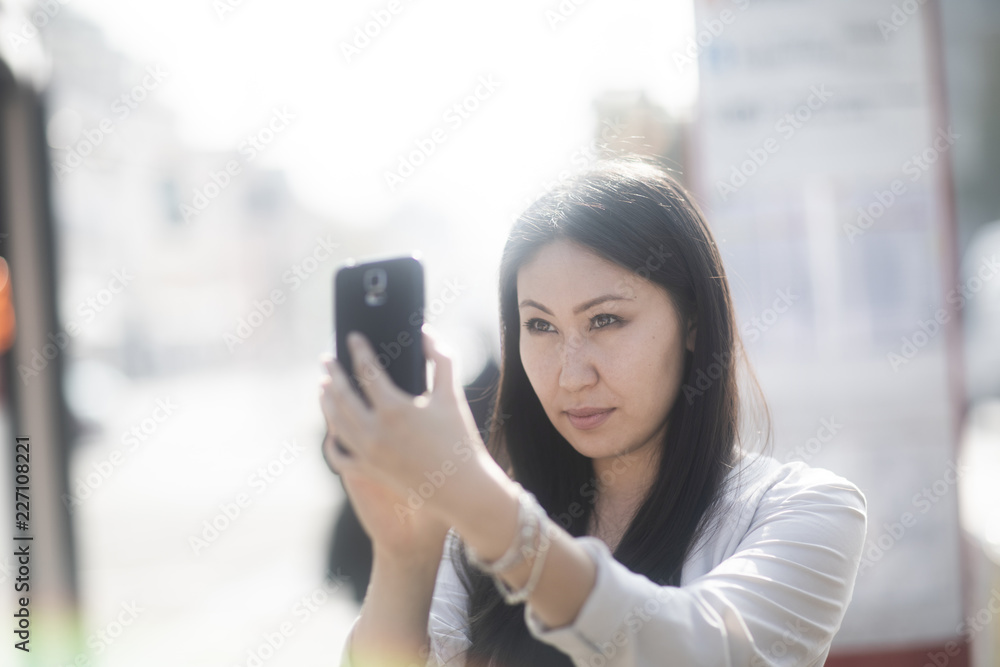 Fototapeta premium Junge Frau Asiatin kauft Ticket mit Smartphone an einer Haltestelle
