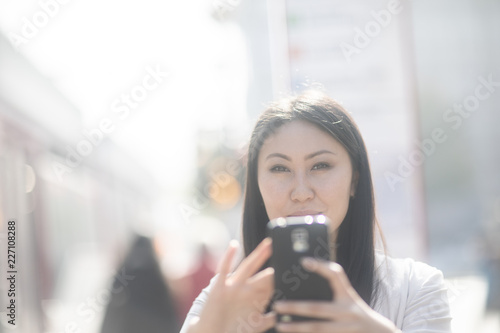 Junge Frau Asiatin kauft Ticket mit Smartphone an einer Haltestelle