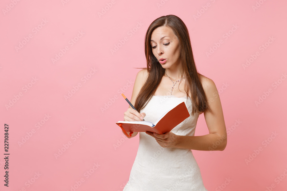 Pensive bride woman in wedding dress planning wedding writing notes in diary, notebook choosing of staff wedding organizers isolated on pink pastel background. Wedding to do list. Celebration concept. Pensive bride woman in wedding dress planning wedding writing notes in diary, notebook choosing of staff wedding organizers isolated on pink pastel background. Wedding to do list. Celebration concept.