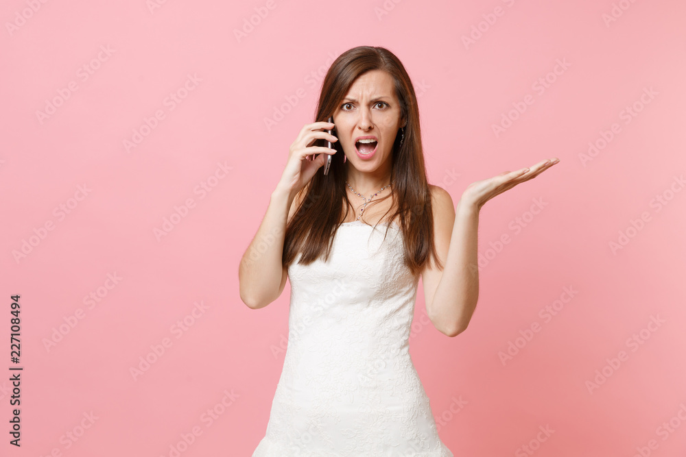 Indignant bride woman in white wedding dress have problem with planning wedding talking on mobile phone, swearing isolated on pastel pink background. Wedding to do list. Organization of celebration. Indignant bride woman in white wedding dress have problem with planning wedding talking on mobile phone, swearing isolated on pastel pink background. Wedding to do list. Organization of celebration.