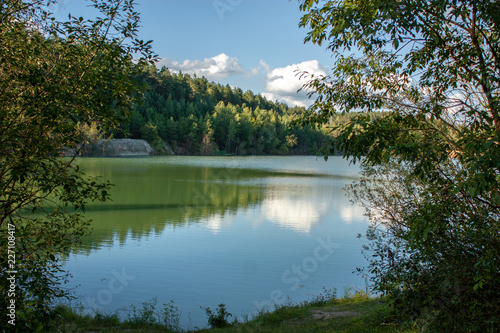 Reflection of forest and white clouds in the blue water of the lake. Summer evening. In the vicinity of Grodno. Belarus.