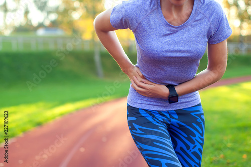 Side stitch - woman runner side cramps after running. Jogging woman with stomach side pain after jogging work out. Female athlete. Sport, health and people concept