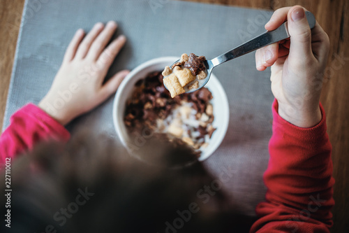 Young girl eating breakfast cereals with milk. Directly above shot, close-up of hands and bowl.