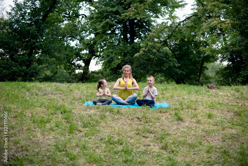 Young happy family doing Yoga relaxation exercises on a grass.