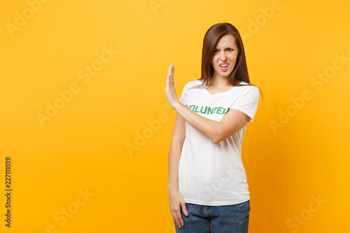 Portrait of sad upset shocked young woman in white t-shirt with written inscription green title volunteer isolated on yellow background. Voluntary free assistance help  charity grace work concept.