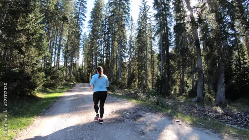 Tracking shot of a woman running in beautiful green forest path in the sun Tracking shot of a woman running in beautiful green forest path in the sun