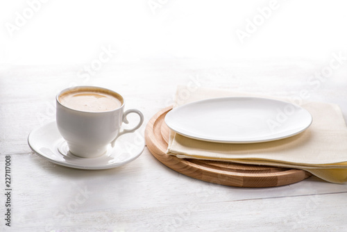 cup of coffee on a light background next to an empty plate for a future layout