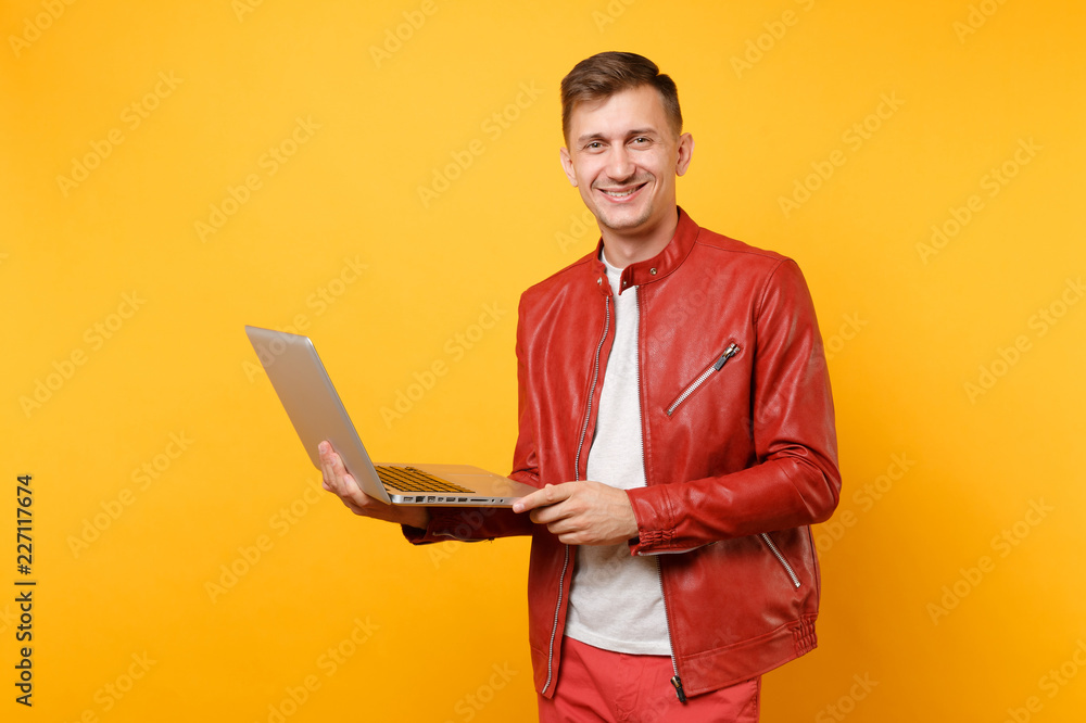 Portrait vogue fun handsome young man in red leather jacket, t-shirt using laptop pc tablet isolated on bright trending yellow background. People sincere emotions lifestyle concept. Advertising area. Portrait vogue fun handsome young man in red leather jacket, t-shirt using laptop pc tablet isolated on bright trending yellow background. People sincere emotions lifestyle concept. Advertising area.