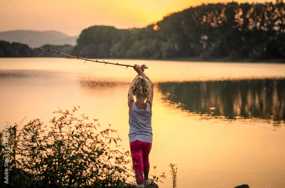 child fishing on the lake at sunset time