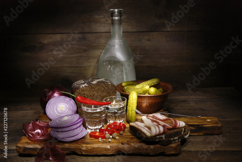 Vodka and snack to it on a wooden background.
