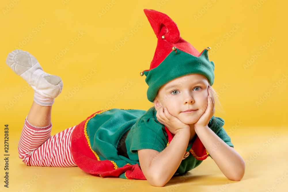 Little girl with blond hair in a Christmas elf costume. The baby is lying  on his stomach. Stock Photo | Adobe Stock