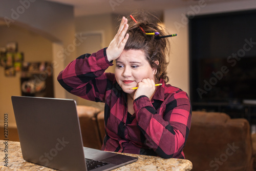 Young white college student slapping forhead in frustration looking at laptop multiple pencils and pens in her hair 