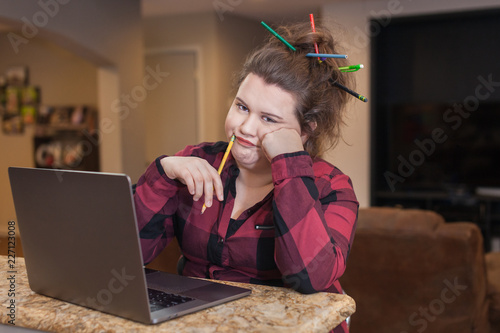 woman working on computer at home college student pencils in hair exhousted over it expression on her face  photo