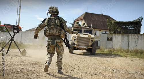 Army soldier directs armoured personnel vehicles in a desert type environment photo