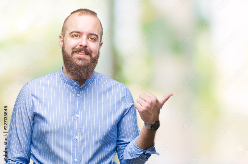 Young caucasian hipster man over isolated background smiling with happy face looking and pointing to the side with thumb up. Young caucasian hipster man over isolated background smiling with happy face looking and pointing to the side with thumb up.