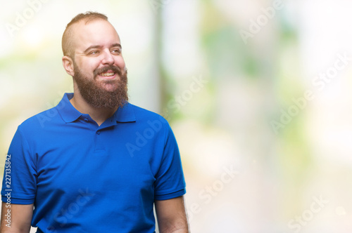 Young caucasian hipster man wearing blue shirt over isolated background looking away to side with smile on face, natural expression. Laughing confident.