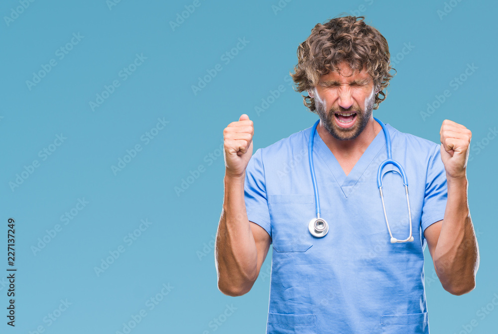 Naklejka premium Handsome hispanic surgeon doctor man over isolated background excited for success with arms raised celebrating victory smiling. Winner concept.