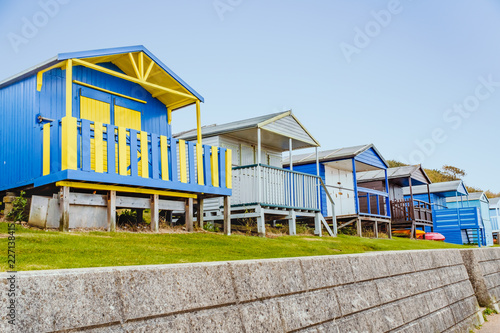Quaint wooden beach huts in a row along a grass verge above a stone wall in Tankerton, Whitstable, Kent, UK photo