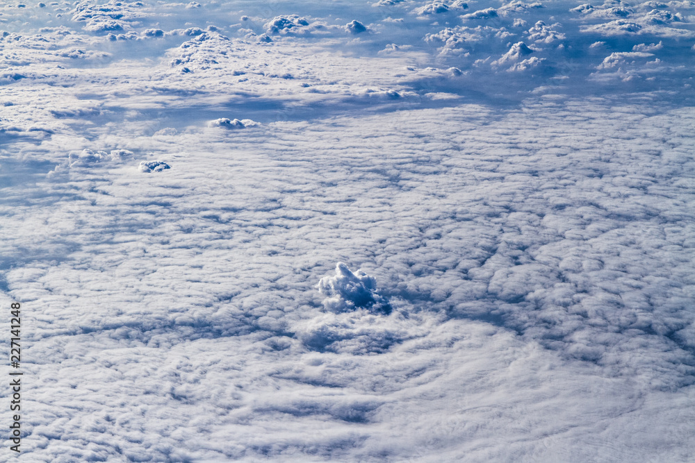 Blue planet Earth sky seen from high above through an airplane window. Unique panoramic high altitude aerial view of a fluffy cotton white cloudscape.